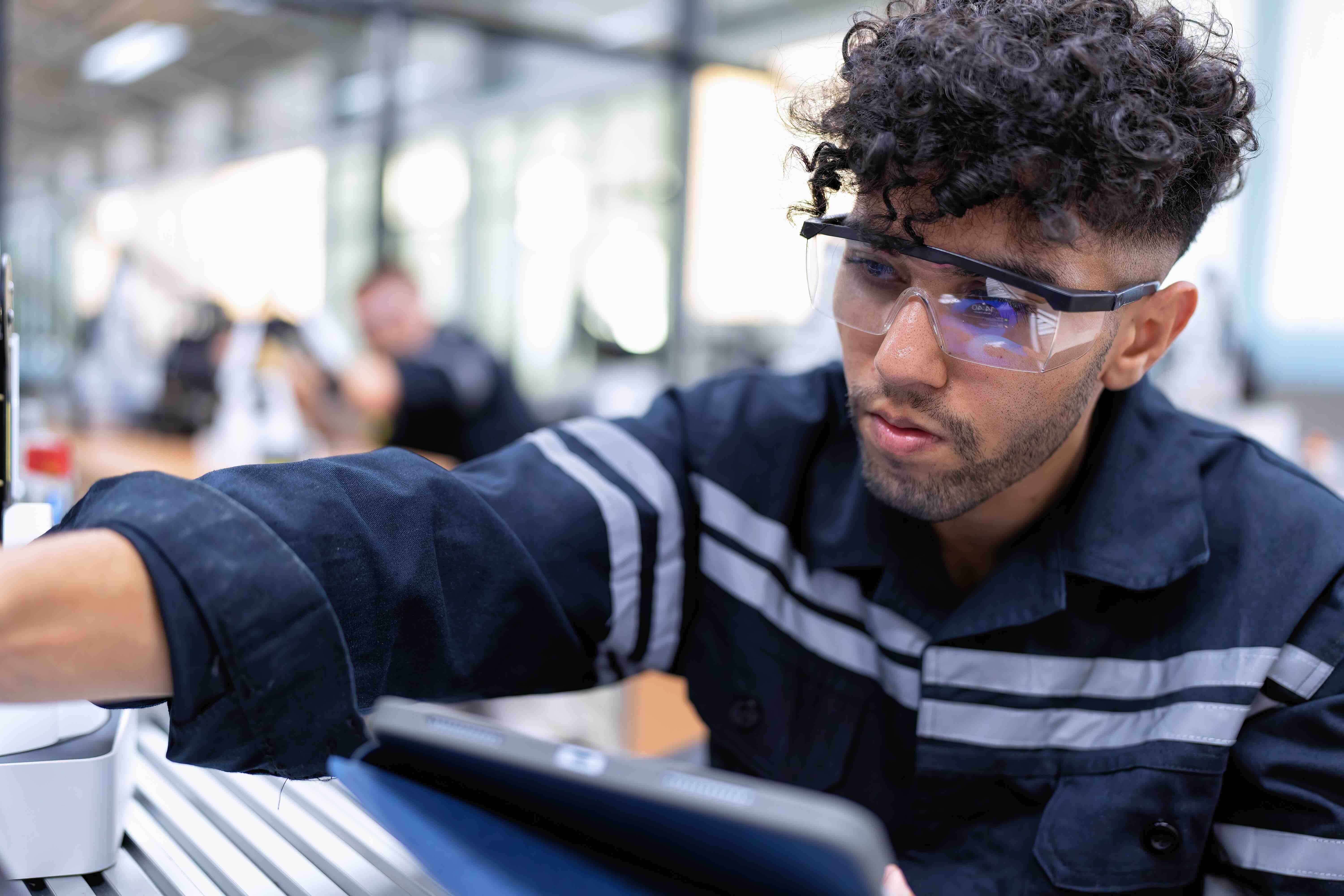 A manufacturing worker using a tablet to inspect production equipment, representing QReserve’s mobile accessibility for on-the-floor asset tracking, real-time maintenance reporting, and instant capacity monitoring.